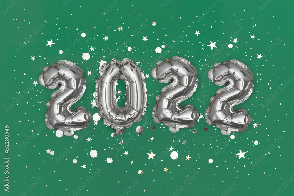 Silver foil balloons numeral 2022 and confetti on gree background. Flat lay Silver foil balloons numeral 2022 and confetti on gree background. Flat lay