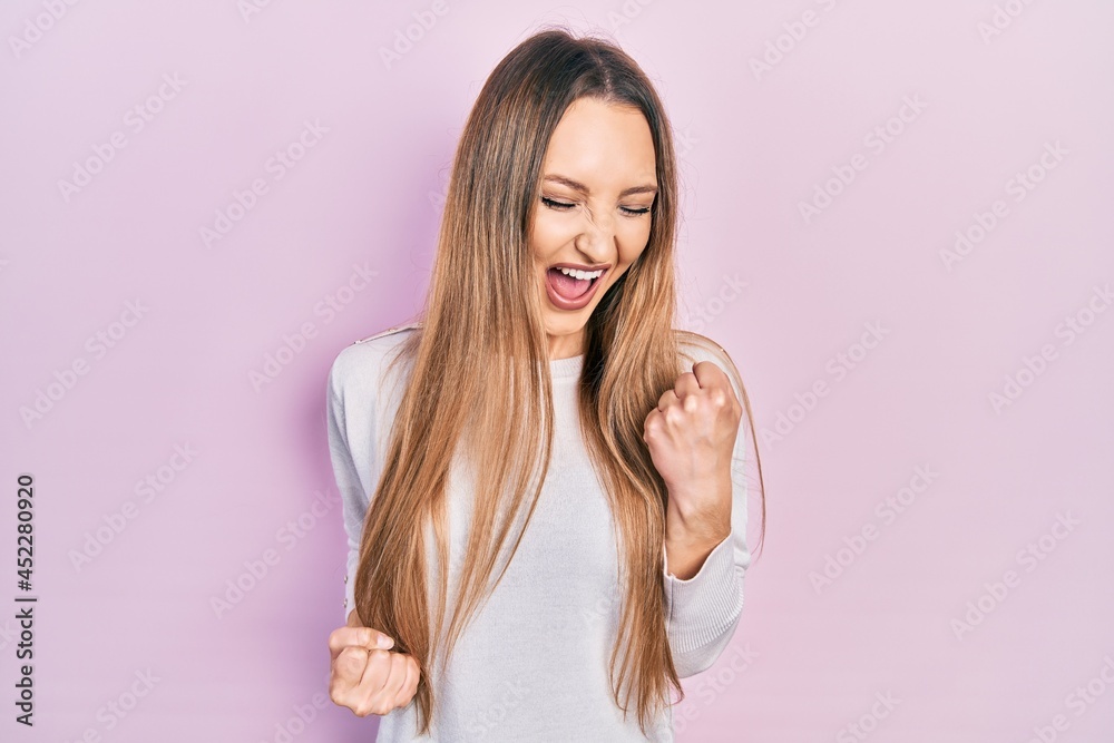 Young blonde girl wearing casual clothes celebrating surprised and amazed for success with arms raised and eyes closed Young blonde girl wearing casual clothes celebrating surprised and amazed for success with arms raised and eyes closed