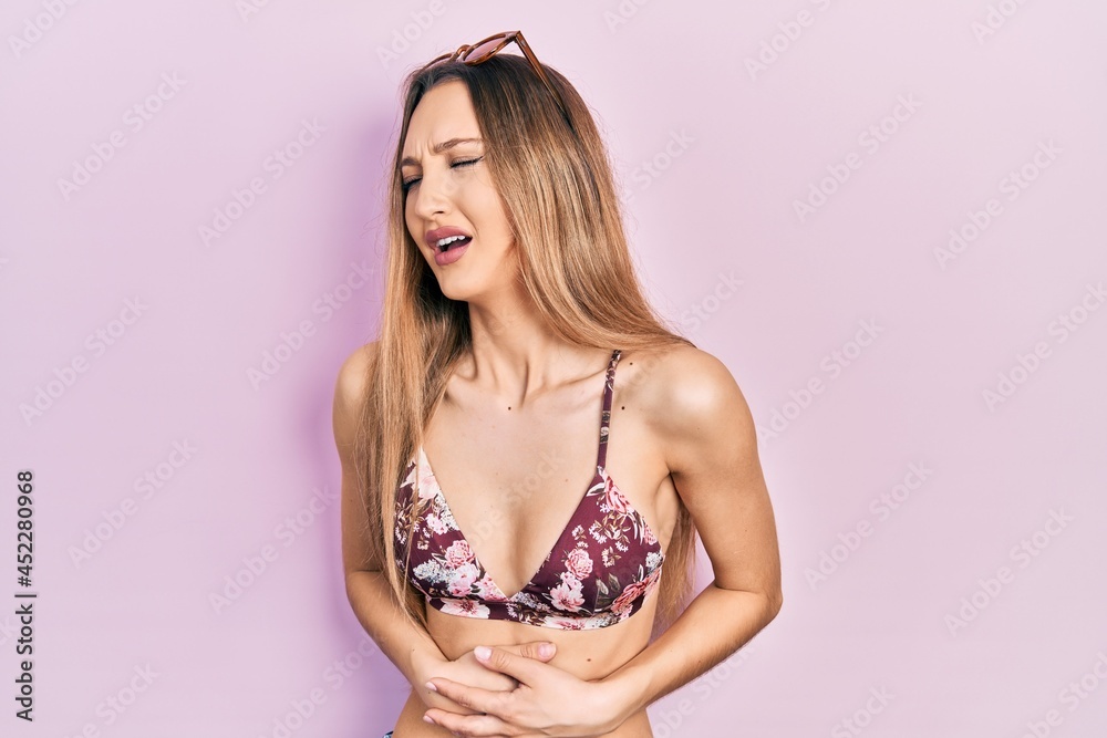 Young blonde girl wearing bikini and sunglasses with hand on stomach because nausea, painful disease feeling unwell. ache concept. Young blonde girl wearing bikini and sunglasses with hand on stomach because nausea, painful disease feeling unwell. ache concept.