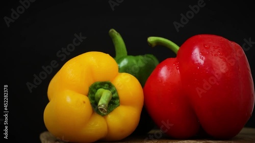Paprika peppers on a black background with water drops. Red, green and yellow sweet bell pepper is rotating video