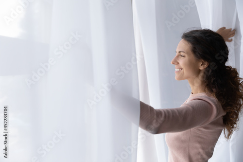 Young Latina woman open curtains at home or hotel looks out window thinking or dreaming, admire view, feels enthusiastic and optimistic, welcoming new sunny day, enjoy peaceful weekend alone concept Free Download Young Latina woman open curtains at home or hotel looks out window thinking or dreaming, admire view, feels enthusiastic and optimistic, welcoming new sunny day, enjoy peaceful weekend alone concept - GFXLoad