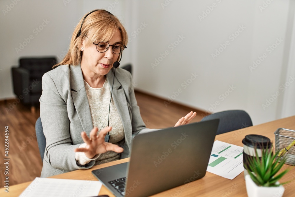 Middle age call center agent having video call using laptop at the office. Middle age call center agent having video call using laptop at the office.