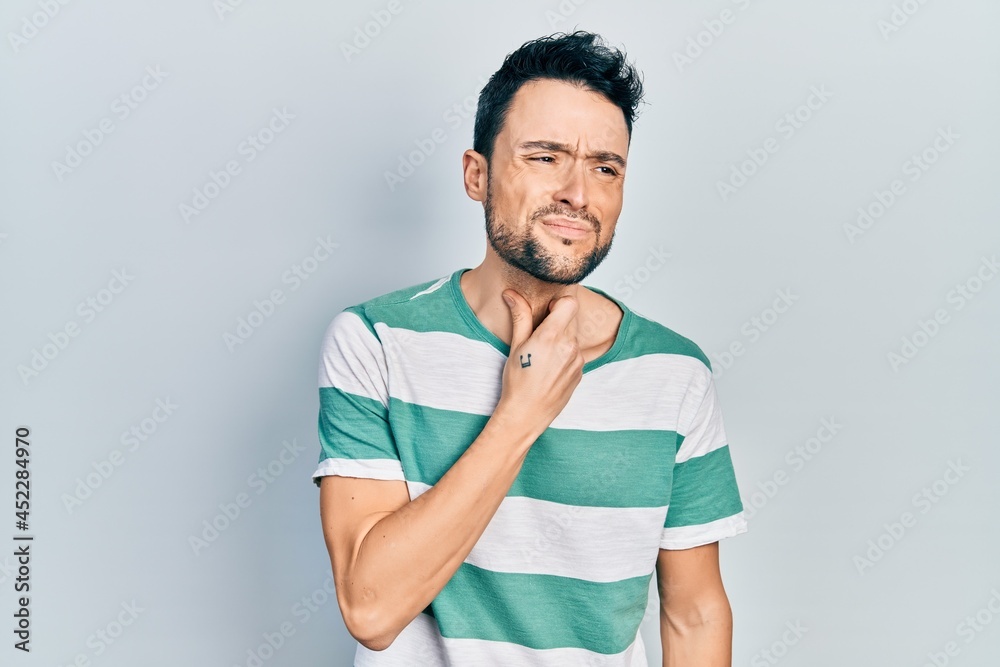 Young hispanic man wearing casual clothes touching painful neck, sore throat for flu, clod and infection Young hispanic man wearing casual clothes touching painful neck, sore throat for flu, clod and infection