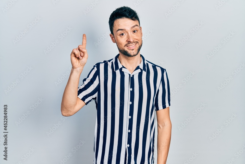Fototapeta premium Young hispanic man wearing casual clothes showing and pointing up with finger number one while smiling confident and happy.
