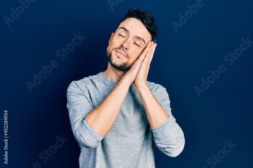 Young hispanic man wearing casual clothes sleeping tired dreaming and posing with hands together while smiling with closed eyes.