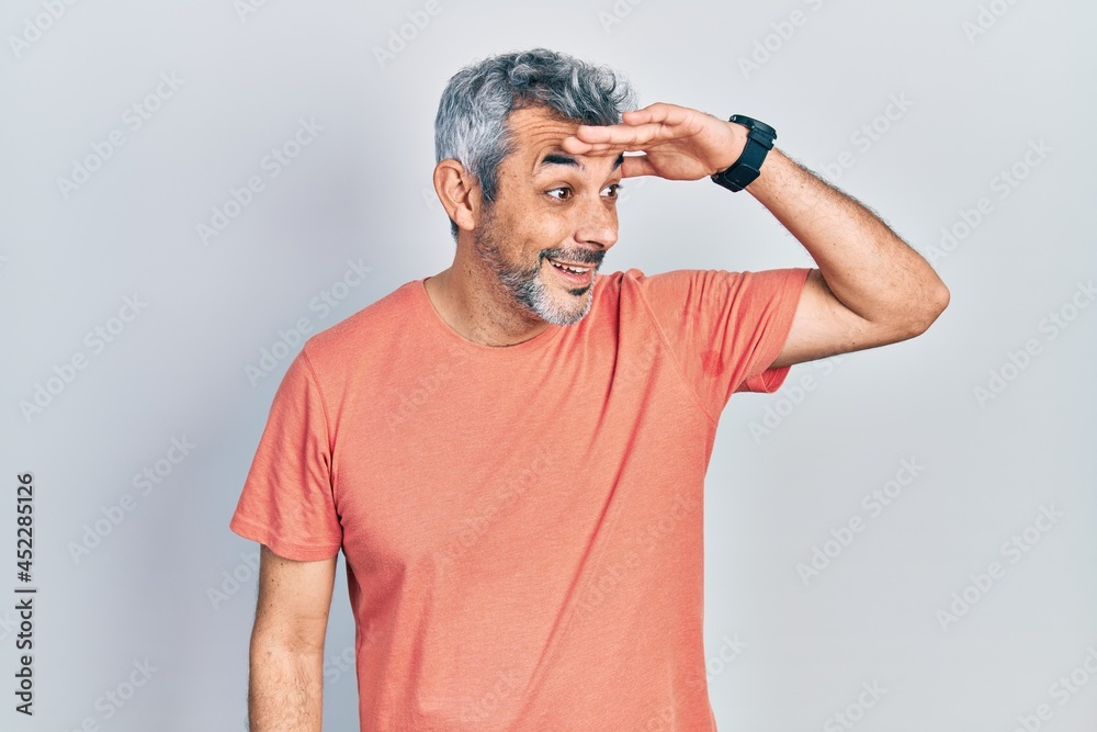 Handsome middle age man with grey hair wearing casual t shirt very happy and smiling looking far away with hand over head. searching concept. Handsome middle age man with grey hair wearing casual t shirt very happy and smiling looking far away with hand over head. searching concept.