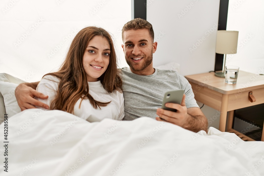 Fototapeta premium Young caucasian couple using smartphone lying on bed at home.