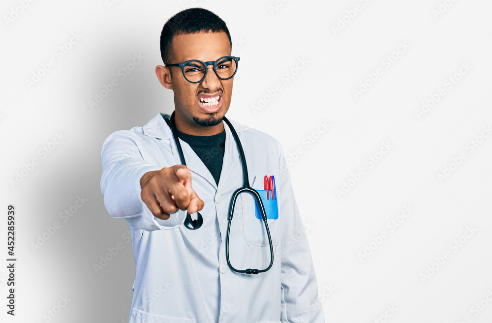 Young african american man wearing doctor uniform and stethoscope pointing displeased and frustrated to the camera, angry and furious with you Young african american man wearing doctor uniform and stethoscope pointing displeased and frustrated to the camera, angry and furious with you