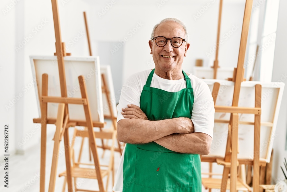 Senior grey-haired artist man smiling happy standing with arms crossed gesture at art studio.