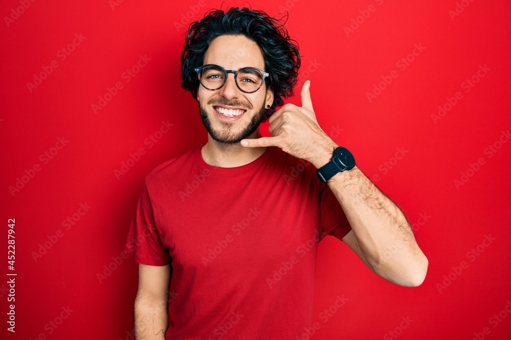 Handsome hispanic man wearing casual t shirt and glasses smiling doing phone gesture with hand and fingers like talking on the telephone. communicating concepts. Handsome hispanic man wearing casual t shirt and glasses smiling doing phone gesture with hand and fingers like talking on the telephone. communicating concepts.