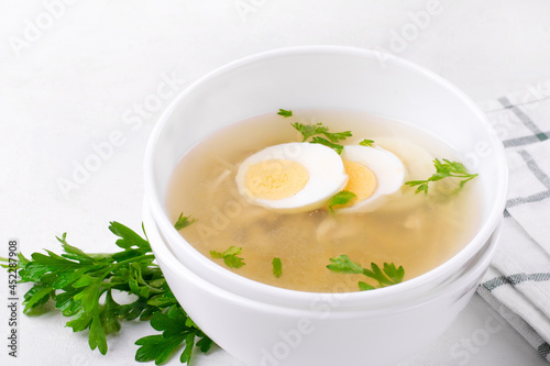 Chicken soup with vermicelli and boiled eggs topped with parsley served in the white bowl. Nutritious hot meal