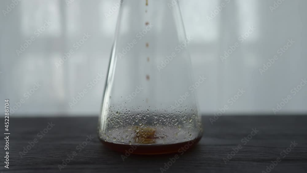 Slow motion cold brew coffee drips in glass carafe on black oak table