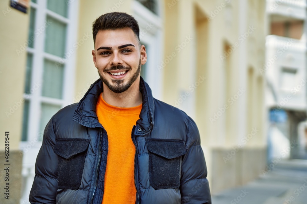 Fototapeta premium Handsome hispanic man with beard smiling happy and confident at the city wearing winter coat