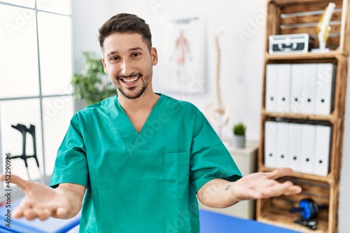 Young physiotherapist man working at pain recovery clinic smiling cheerful offering hands giving assistance and acceptance.