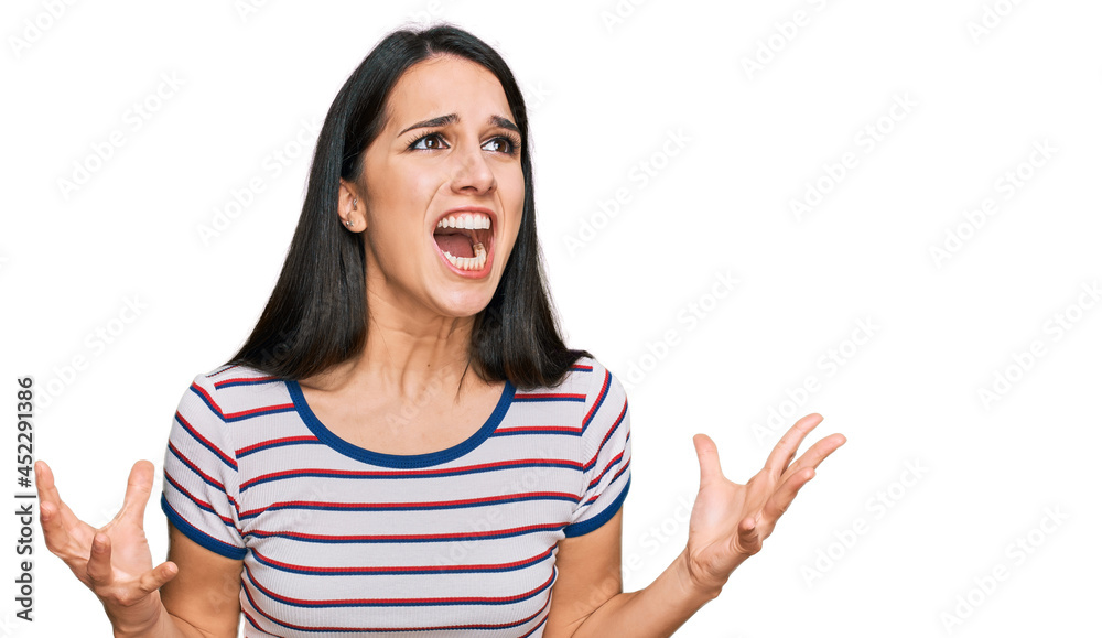 Young hispanic girl wearing casual striped t shirt crazy and mad shouting and yelling with aggressive expression and arms raised. frustration concept. Young hispanic girl wearing casual striped t shirt crazy and mad shouting and yelling with aggressive expression and arms raised. frustration concept.