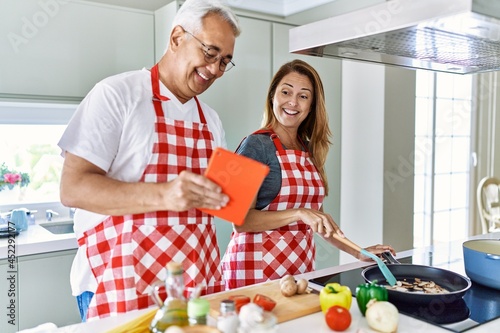 Middle age hispanic couple smiling happy cooking and using touchpad at the kitchen.