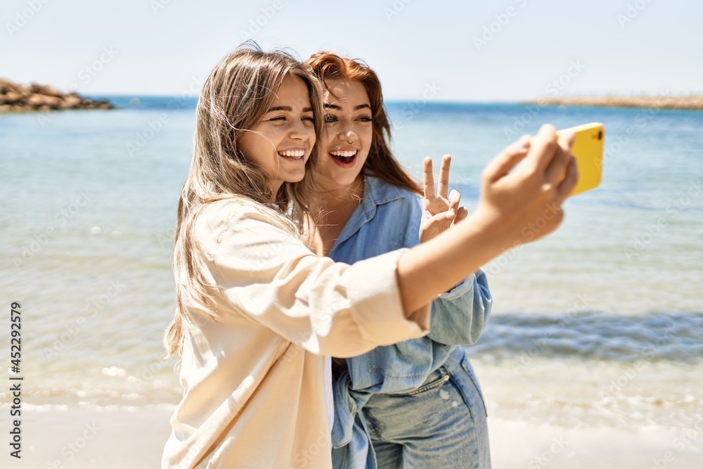 Young lesbian couple of two women in love at the beach. Beautiful women together at the beach in a romantic relationship taking selfie photo with smartphone