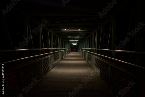 A nightly photographed bridge in an nostalgic look with a person walking far at the end of the bridge (ID: 452292929)
