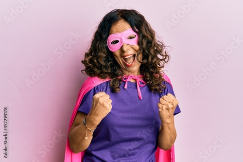 Middle age hispanic woman wearing super hero costume celebrating surprised and amazed for success with arms raised and eyes closed