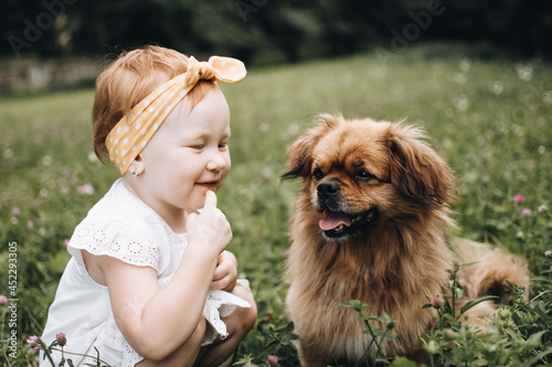 Cute red headed girl with her red haired dog in the summer park. Child and the pet. Little friend.