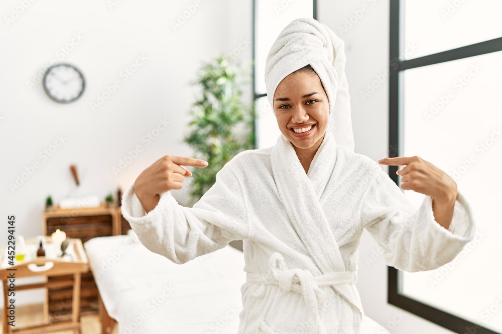Young brunette woman wearing towel and bathrobe standing at beauty center looking confident with smile on face, pointing oneself with fingers proud and happy. Young brunette woman wearing towel and bathrobe standing at beauty center looking confident with smile on face, pointing oneself with fingers proud and happy.