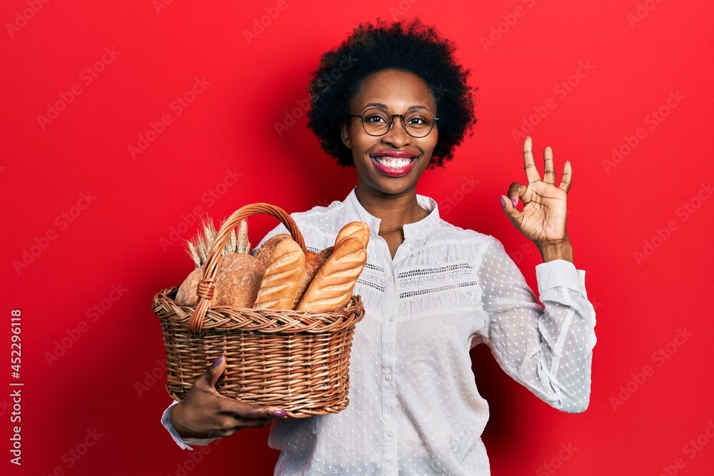 Young african american woman holding wicker basket with bread doing ok sign with fingers, smiling friendly gesturing excellent symbol Young african american woman holding wicker basket with bread doing ok sign with fingers, smiling friendly gesturing excellent symbol