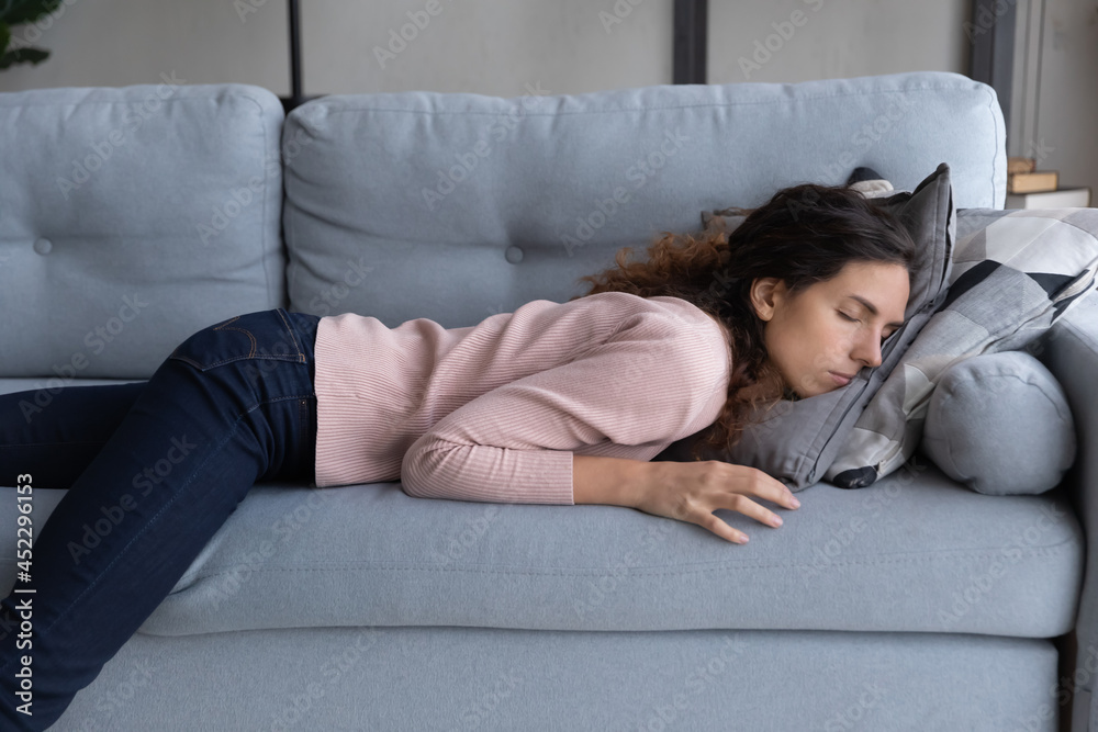 Exhausted young woman lying on sofa sleeping at end of hard workday, after  hard-working day. Tired female fall asleep on couch face in cushion.  Fatigue relief, no motivation, sleepless night concept Stock