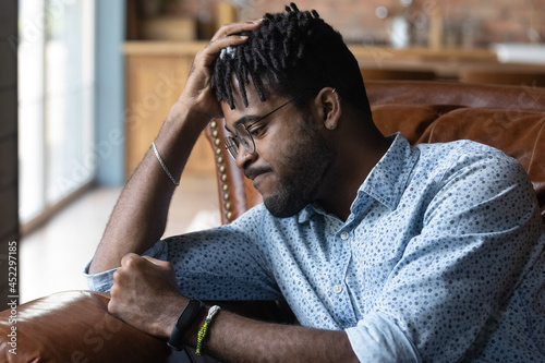 Frustrated disappointed Black guy feeling anger, regret about lost opportunities. Young African man suffering from negative mood, depression at home, beating couch with fist