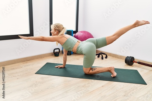 Young blonde girl smiling happy stretching at sport center.