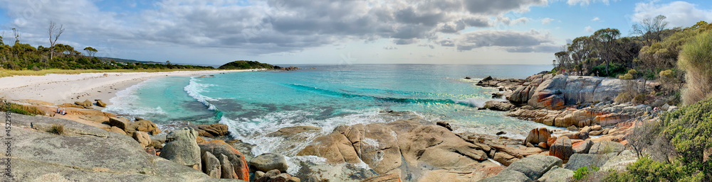 Panorama of beach with turquoise water, cloudy blue sky, orange rocky shoreline. Bay of Fires, Tasmania, Australia. No people
