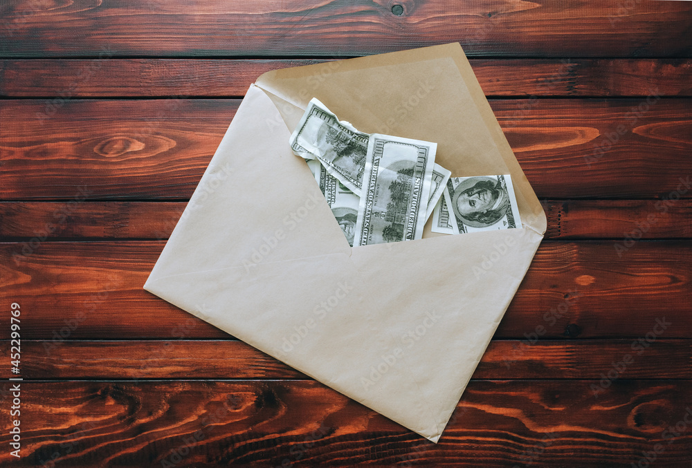 Fototapeta premium A large craft beige envelope with dollar bills lies on a brown table. The concept of a bribe, donation, alimony. View from above.