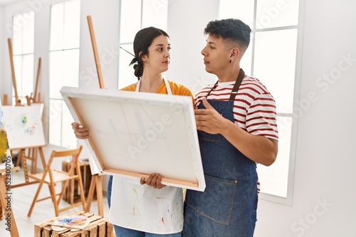Two hispanic paint students holding canvas at art studio.