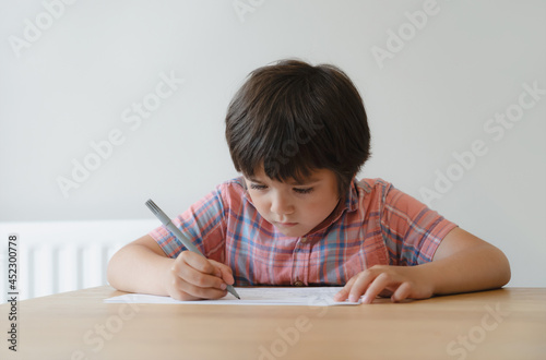 Schoolboy using pencil drawing on white paper sheet, Young kid doing school homework, Happy mixed race child enjoy doing arts and crafts at home on weekend. Home schooling, Education concept