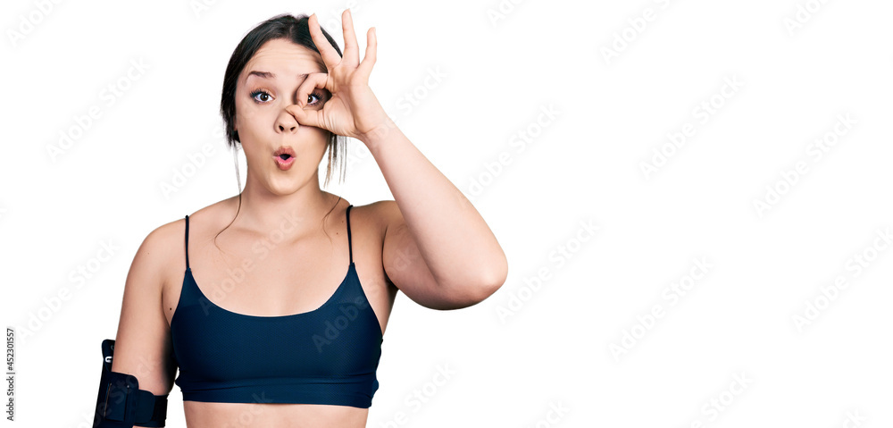 Young hispanic woman wearing sportswear doing ok gesture shocked with surprised face, eye looking through fingers. unbelieving expression. Young hispanic woman wearing sportswear doing ok gesture shocked with surprised face, eye looking through fingers. unbelieving expression.
