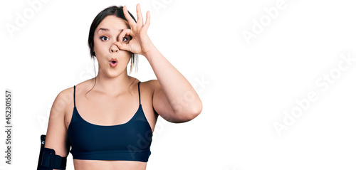 Young hispanic woman wearing sportswear doing ok gesture shocked with surprised face, eye looking through fingers. unbelieving expression.