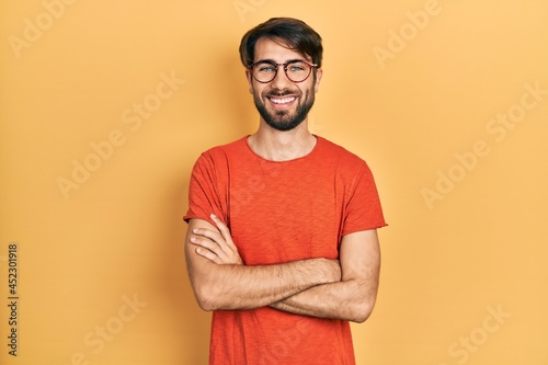 Young hispanic man wearing casual clothes and glasses happy face smiling with crossed arms looking at the camera. positive person.