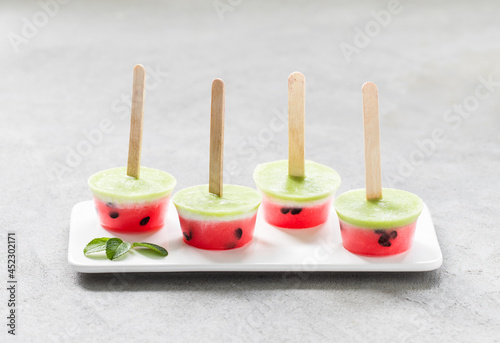 Mini watermelon ice cream with kiwi on a wooden stick on a ceramic plate on a light background