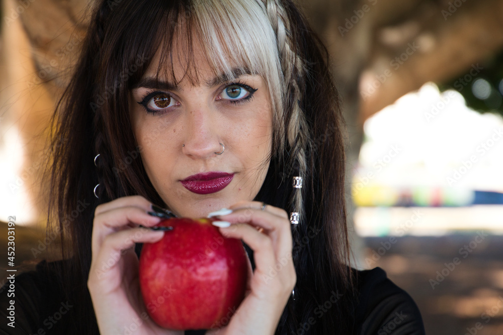 punky girl with blonde and brunette hair holds a red apple in her hands and stares at it. The girl is a witch from the fairy tale. punky girl with blonde and brunette hair holds a red apple in her hands and stares at it. The girl is a witch from the fairy tale.