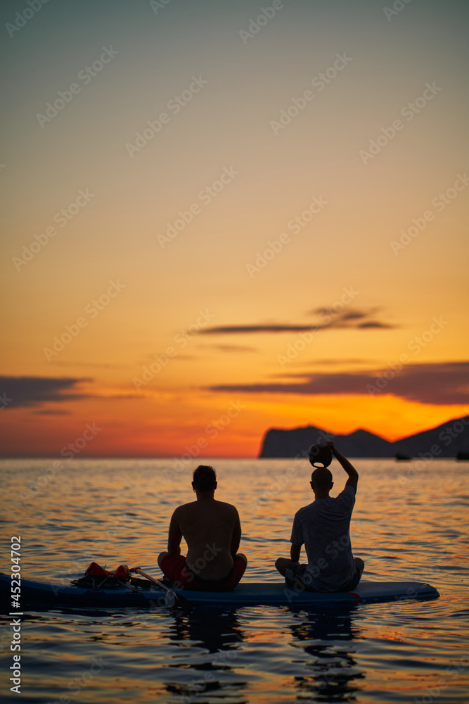 Silhouette of two friends contemplating sunset over Dragonera island