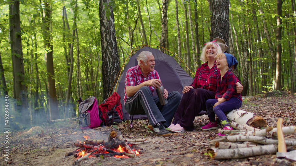 Senior elderly grandmother grandfather granddaughter telling funny stories  fairy tales over campfire in wood. Old man woman and child girl kid  tourists having camping in forest. Active rest of family Stock Photo |
