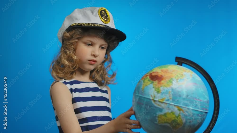 Little girl in sailor hat is pointing finger into the globe on a blue background Little girl in sailor hat is pointing finger into the globe on a blue background