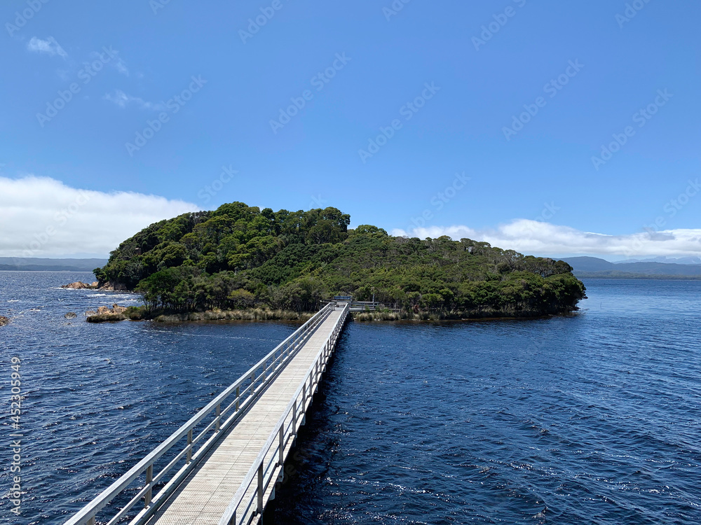 jetty leading to an island in the macquarie harbour. Historic site, solitude, lonely island in the middle of a body of water. blue sky. No people, copy space.