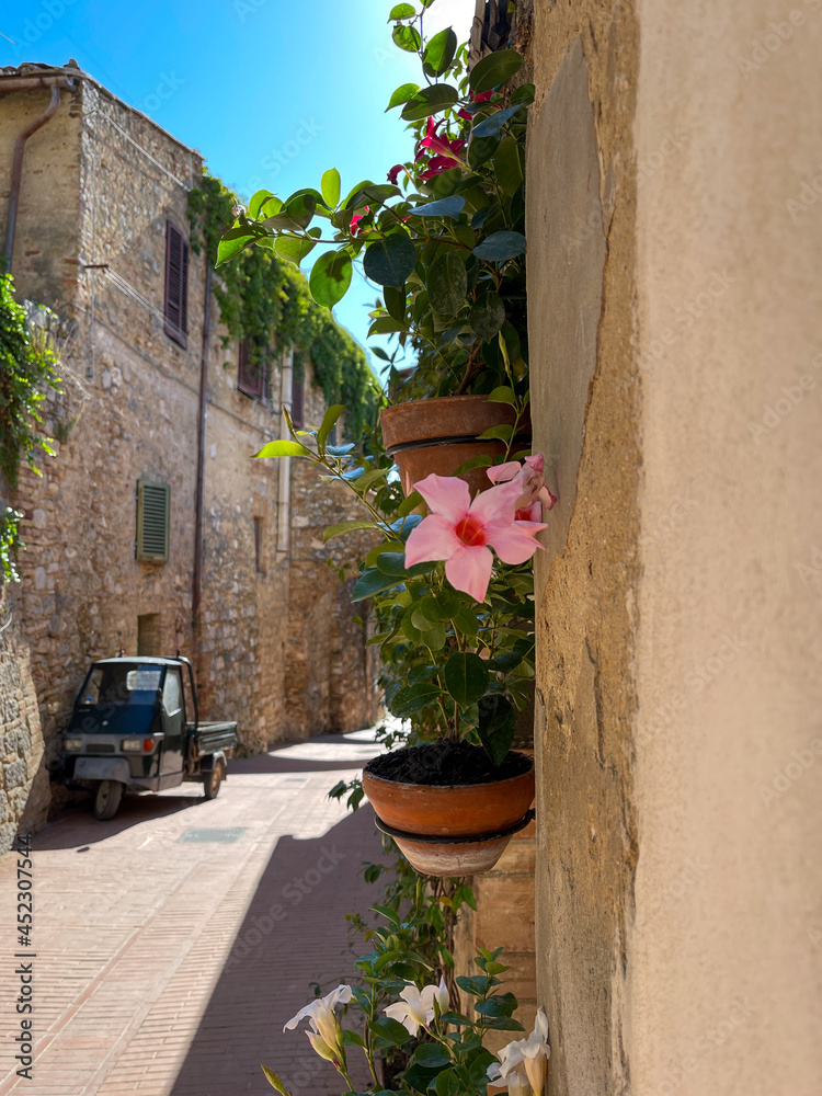 Naklejka premium Ein verschlaffenes Dorf in Italien, bunte Blumen an der Wand mit einem kleinen Fahrzeug im Hintergrund.