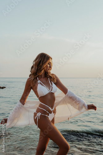 beautiful woman with blond hair in elegant bikini posing on the sunset beach