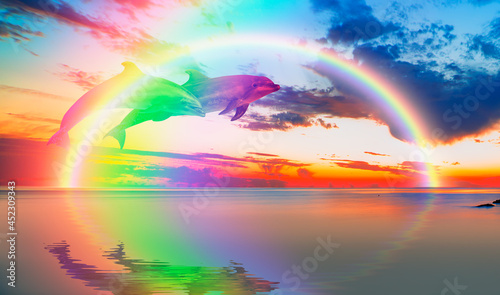 Two dolphins in rainbow colors jumping on the water with amazing rainbow in the background at sunset