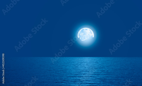 Night sky with full bright moon in the clouds, blue sea in the foreground "Elements of this image furnished by NASA"