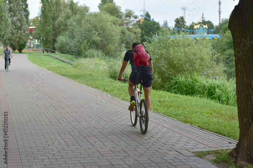 The photo shows a young athlete riding a bicycle along a park track. © Михаил Жигалин