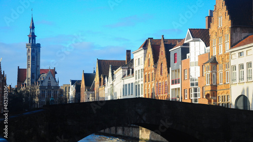Bruges cityscape. The old, medieval houses are placed near a canal. A church with a bell tower can be seen in background. Belgium © Alexandru V