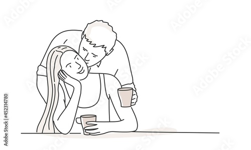 Man kissing smiling woman sitting at home or in cafe and holding mug in hands.