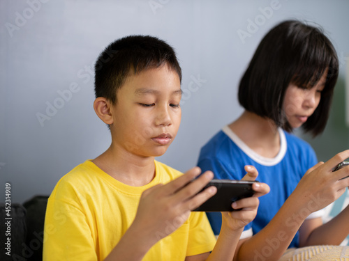 children sit on couch in living room holding smart phone, chatting use social media network, watch received video from friend, with modern wireless technology.